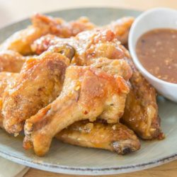 Honey Garlic Chicken Wings Piled on a Plate with ramekin of Dipping Sauce