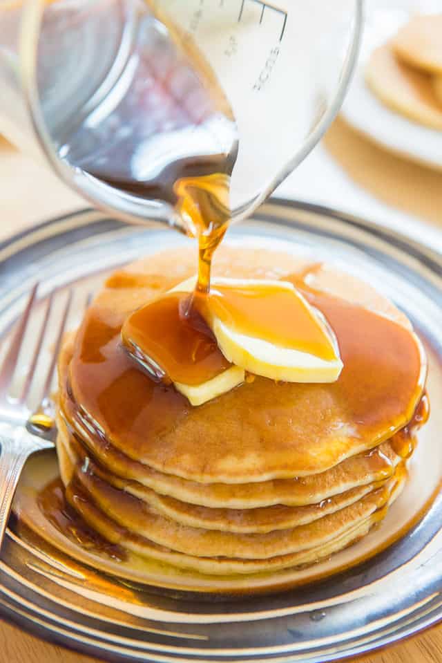 Buttermilk Pancake Recipe Shown In a Stack on Plate with Butter Pats and Syrup Pouring On Top