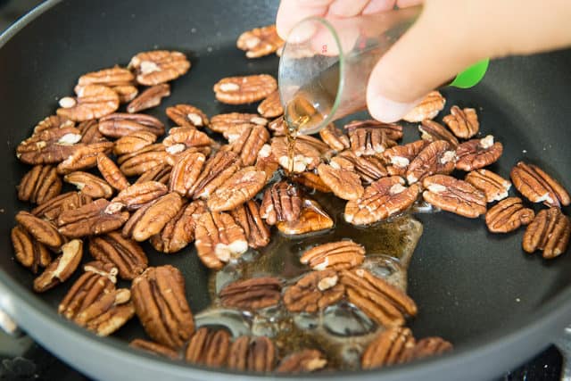 Pouring Maple Syrup Over Toasted Pecans in a Nonstick Skillet