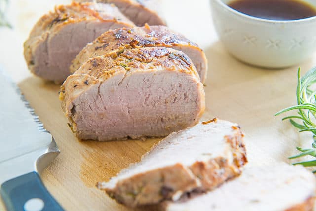 Oven Roasted Pork Tenderloin - Sliced and Served on Wooden Cutting Board with Bowl of Juices