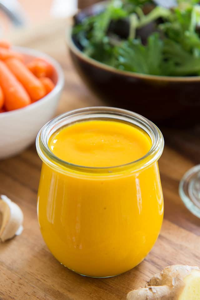 Carrot Ginger Dressing - In a Glass Jar on a Wooden Board with Salad in Background