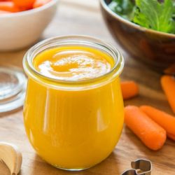 Carrot Ginger Dressing In a Glass Jar on a Wooden Board with Salad in Background
