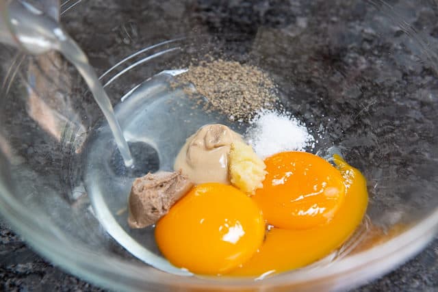 Caesar Dressing Ingredients - In Glass Bowl with Egg Yolks, Mustard, Anchovy Paste, Garlic, salt, Pepper, and Lemon