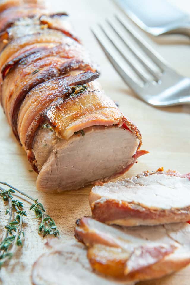 Bacon Wrapped Pork Tenderloin - Sliced on a Wooden Board with Thyme