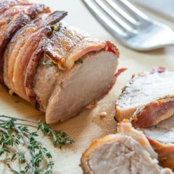 Bacon Wrapped Pork Tenderloin Sliced on a Wooden Board with Thyme