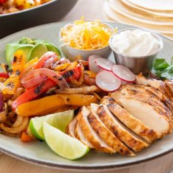 Chicken Fajitas On a Plate with Cheese, Sour Cream, and Lime Wedges