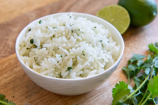 A small white bowl filled with cilantro lime rice with fresh lime rounds on the side