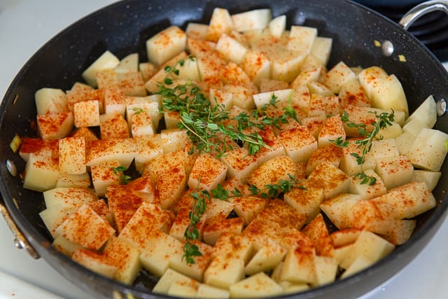Bite-size chunks of peeled russet potatoes in skillet with spices and fresh thyme