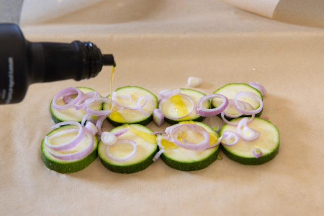 Zucchini Slices on Parchment Paper Topped with Shallot Slices and Olive Oil
