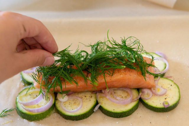 Adding Fresh Dill On To Salmon Fillet on Parchment Paper