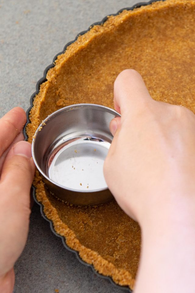 Graham Cracker Crust - Being Pressed Into a Tart Pan Using Measuring Cup