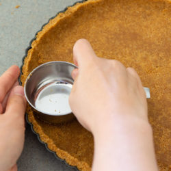 Graham Cracker Crust Being Pressed Into Tart Pan with Measuring Cup