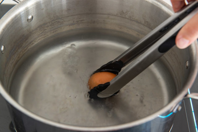 Gently Placing a Brown Egg Into Boiling Water with Tongs