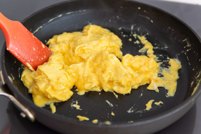 Almost Fully Scrambled Eggs in Skillet Stirring with Red Spatula