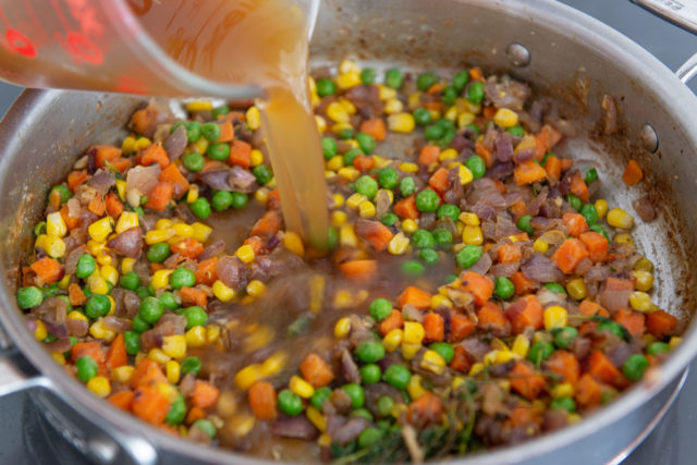 Pouring beef stock into pan with vegetables