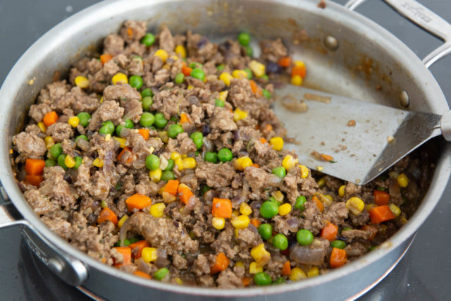 Ground lamb with peas, carrots, corn, and onion in a skillet