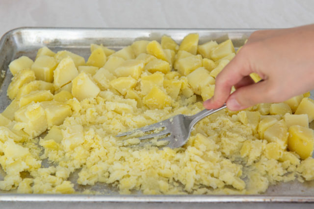 Mashing Yukon Gold Potato Chunks with Fork on a Sheet Pan