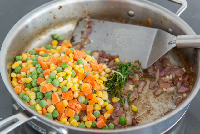 Frozen veggie medley with peas, carrots, and corn added to softened onions in skillet
