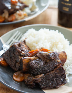 Slow Cooker Beef Short Ribs Plated with White Rice and a Fork with Wine in Back