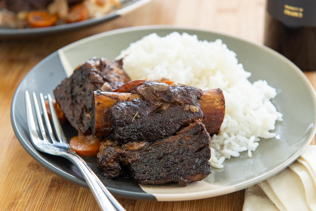 Slow Cooker Beef Short Ribs Plated with White Rice and a Fork with Wine in Back