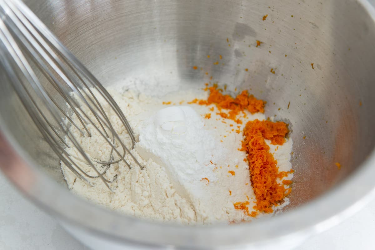 Flour, baking powder, salt, and orange zest in a bowl with a whisk