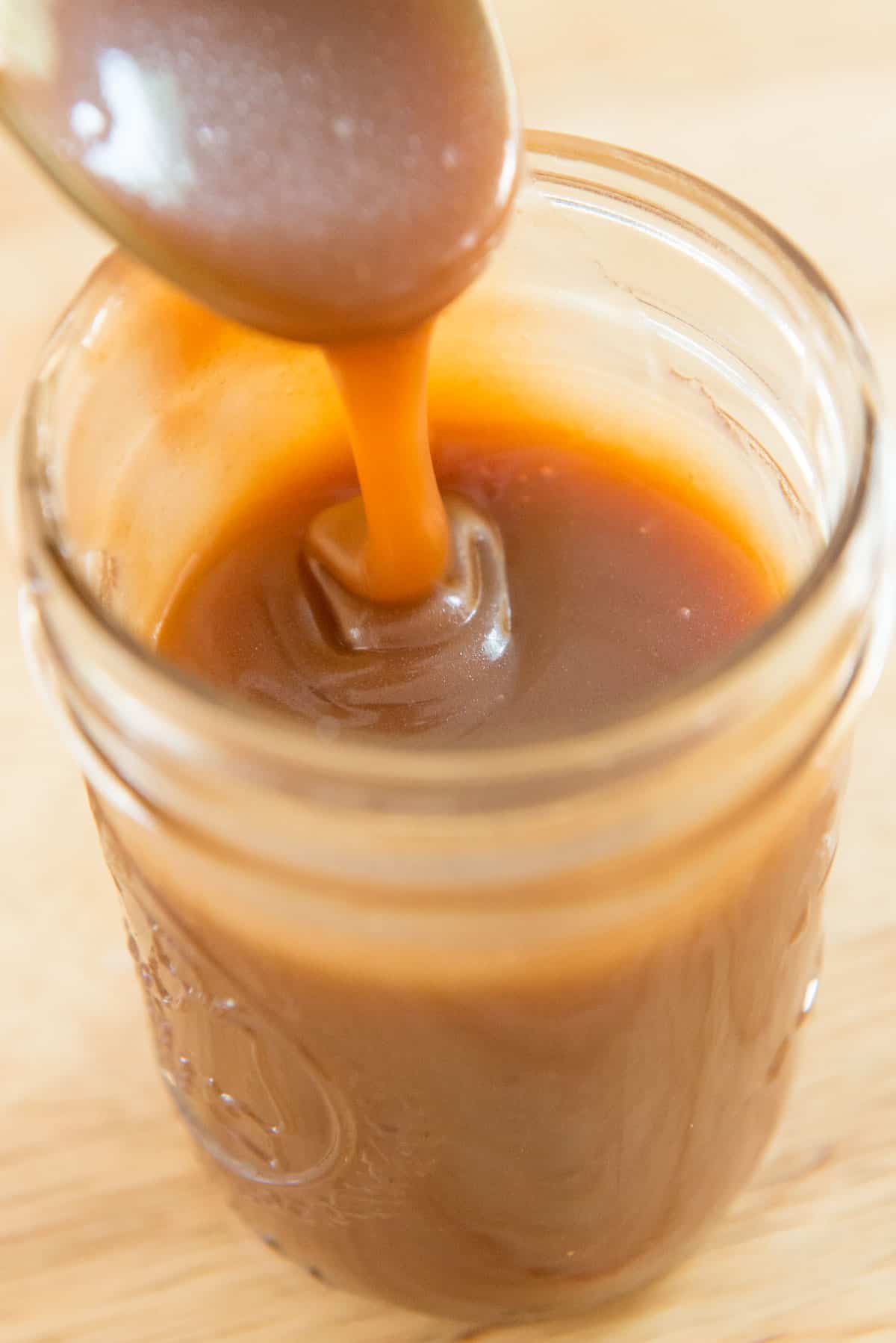 spoon drizzling homemade caramel sauce into a jar
