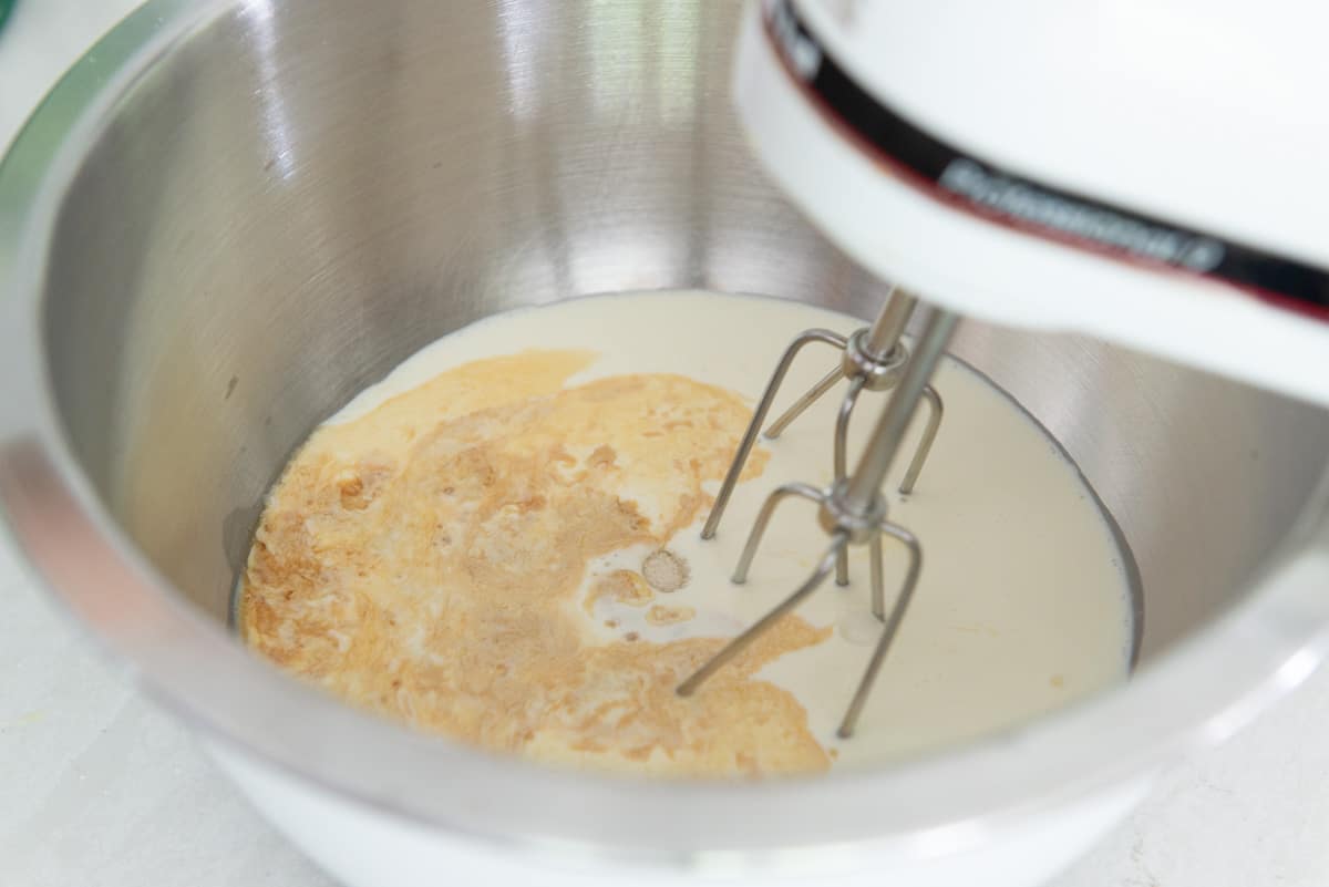 An electric hand mixer with beaters in a bowl with cream and vanilla