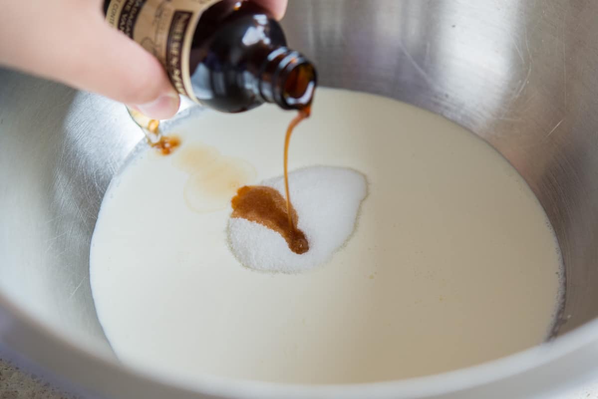 Pouring vanilla extract into the mixing bowl with sugar and cream