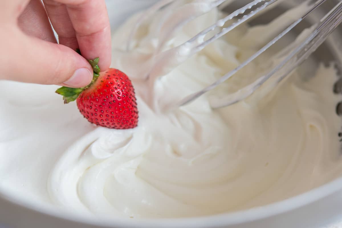 A strawberry dipped into a bowl of homemade whipped cream