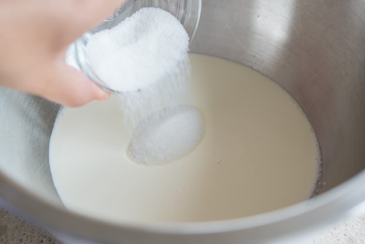 Pouring granulated white sugar into a bowl of heavy cream