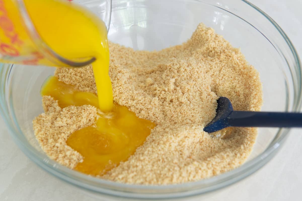 Vanilla cookie crumbs in a glass mixing bowl with melted butter pouring in