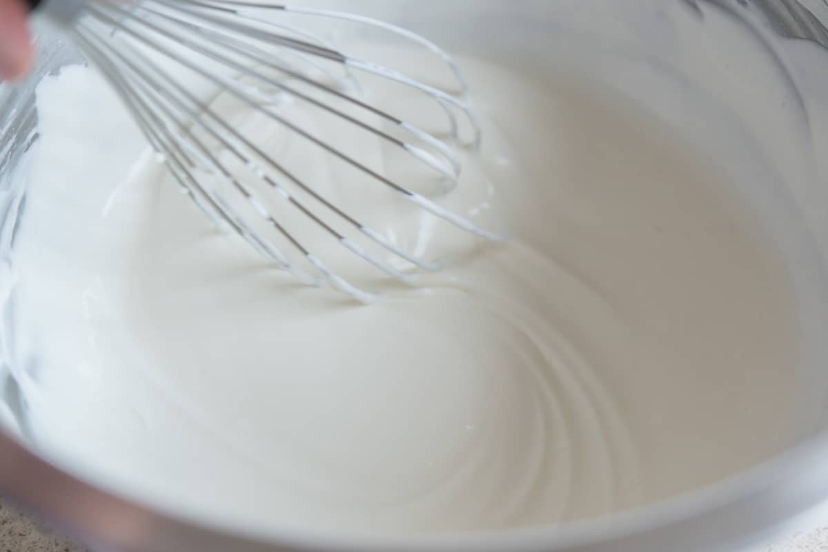 A whisk in a bowl of whipped cream showing the thickness