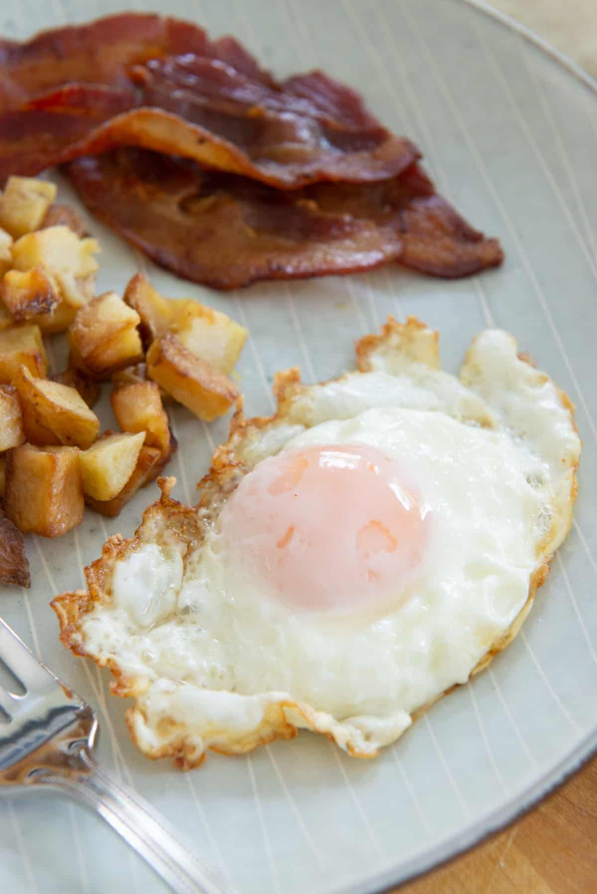 A Basted Egg from Bacon Grease On A Plate with Potatoes and Bacon