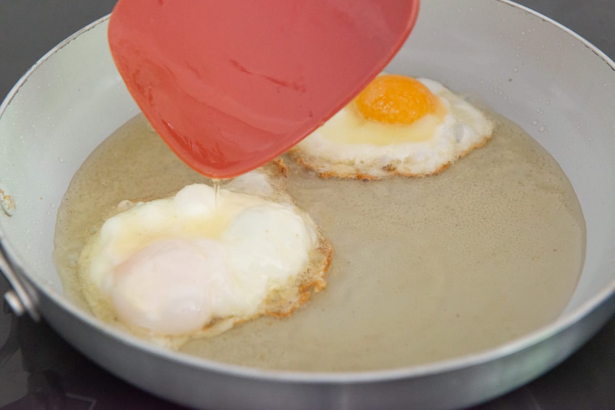 Basting an egg with bacon fat in a pan