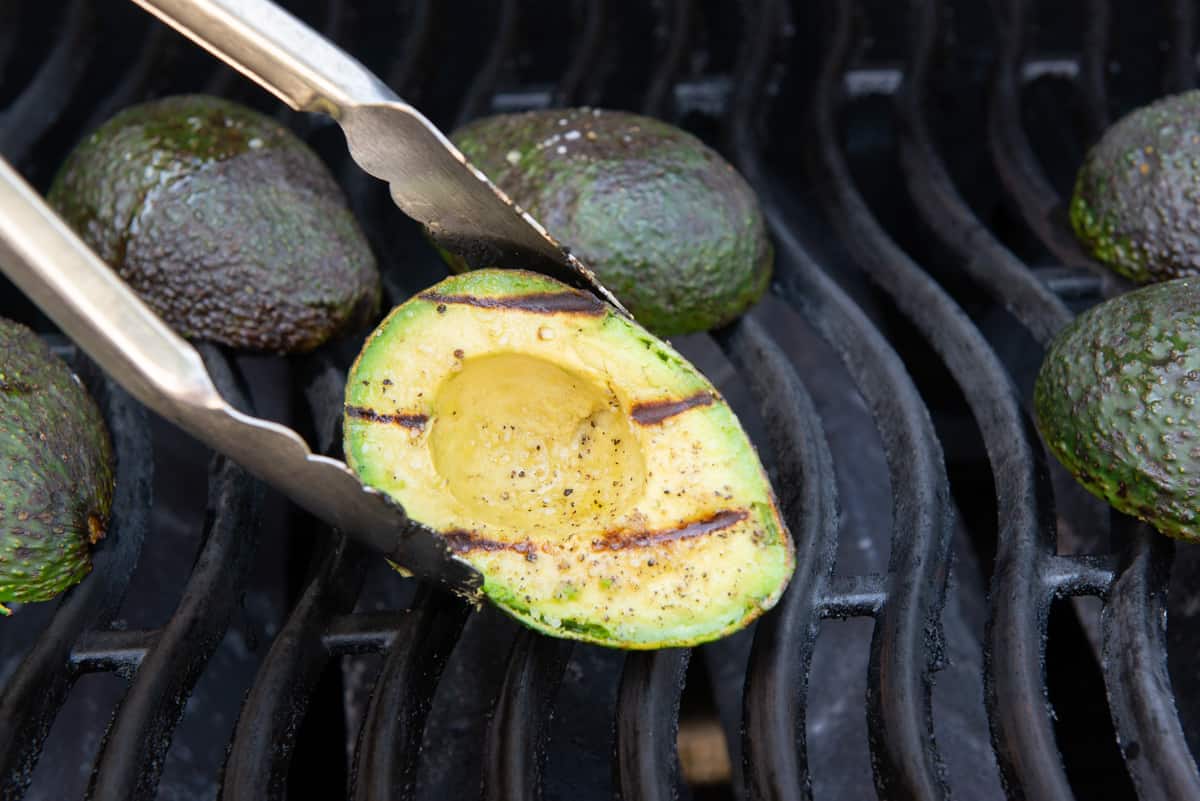 A Grilled Avocado Half with Tongs Showing Grill Marks