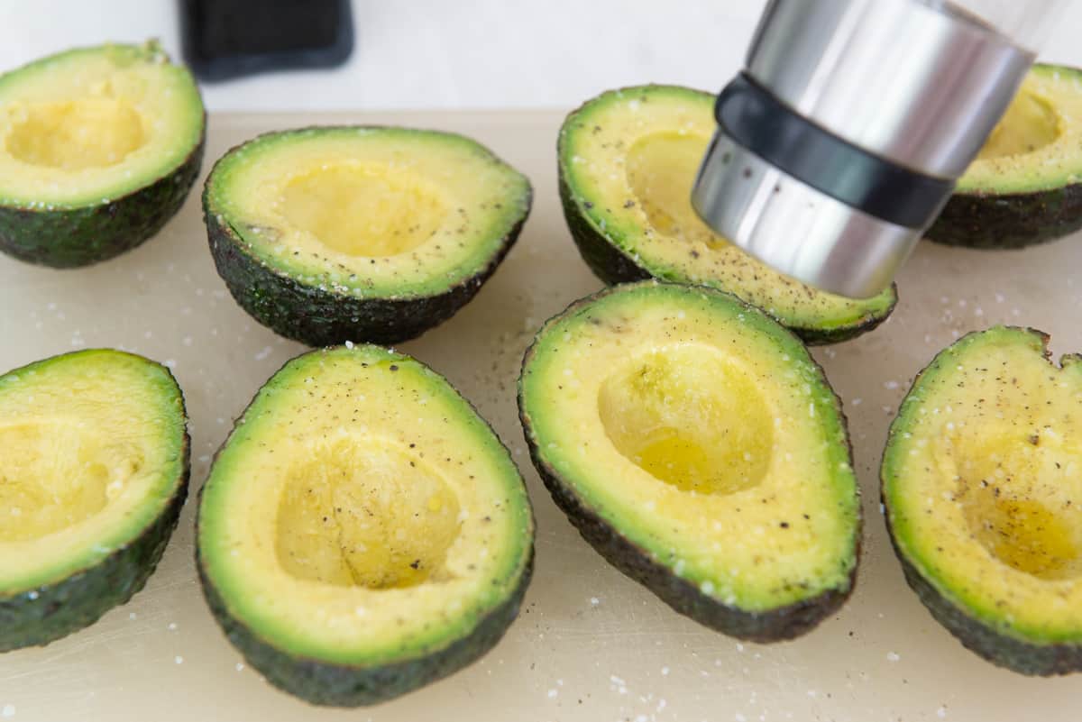 Grinding Fresh Black Pepper Onto A Cutting Board with Avocado Halves