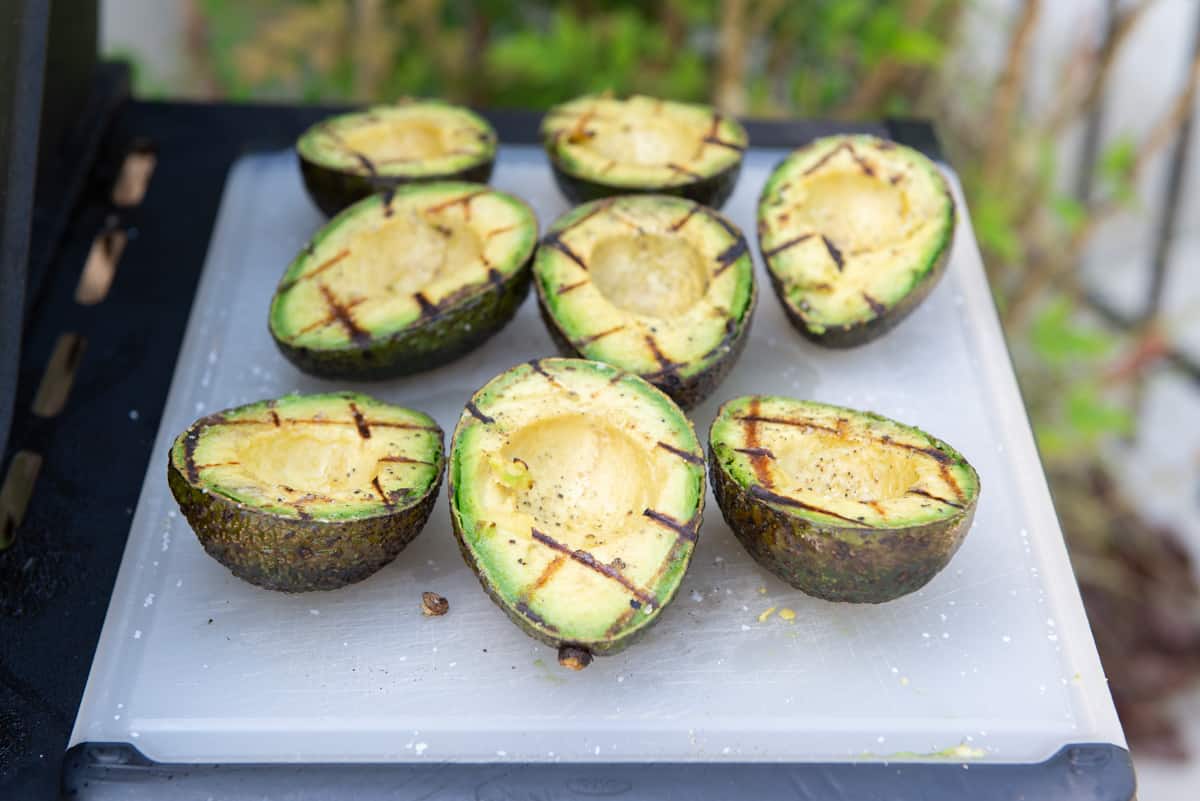 A Cutting Board On Grill Shelf with Grilled Avocados