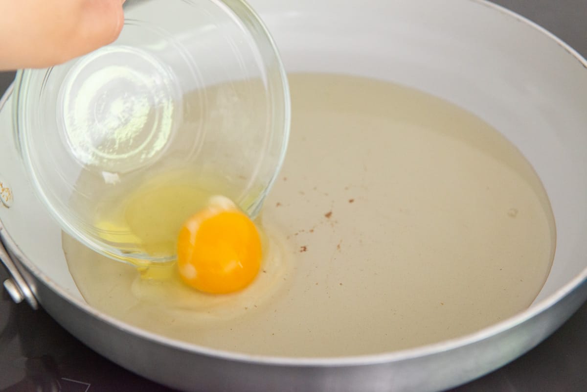 Pouring an egg from a bowl into a pan of bacon fat