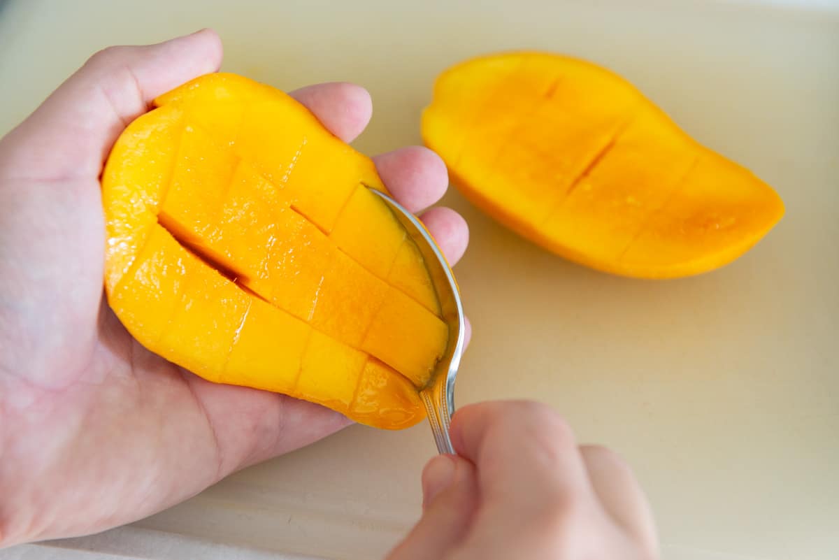 Scooping Mango Cubes from Skin with Spoon
