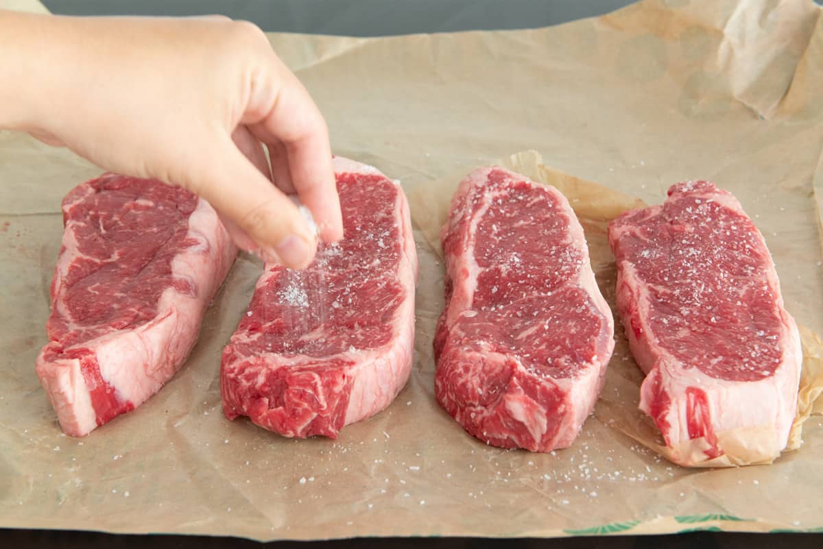 Seasoning 4 NY Strip Steaks On Butcher Paper With Salt