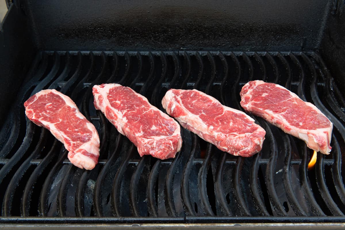 4 NY Strip Steaks On Grill Grates Of Gas Grill