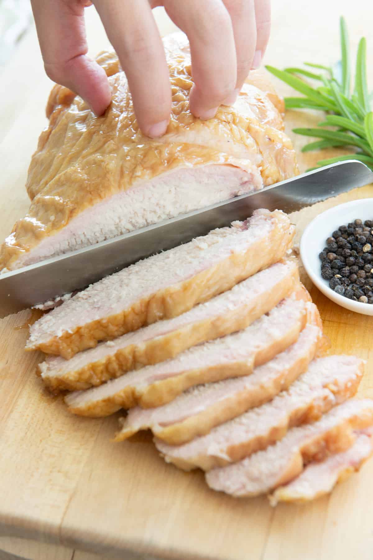 Slicing Smoked Turkey Breast On Wooden Cutting Board With Serrated Knife