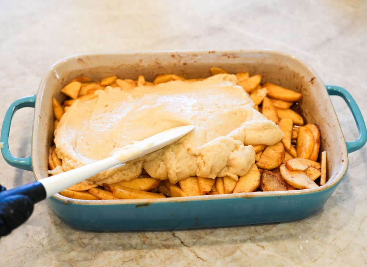 Baking dish with cinnamon sugar coated apples with cobbler biscuit being spread over the top