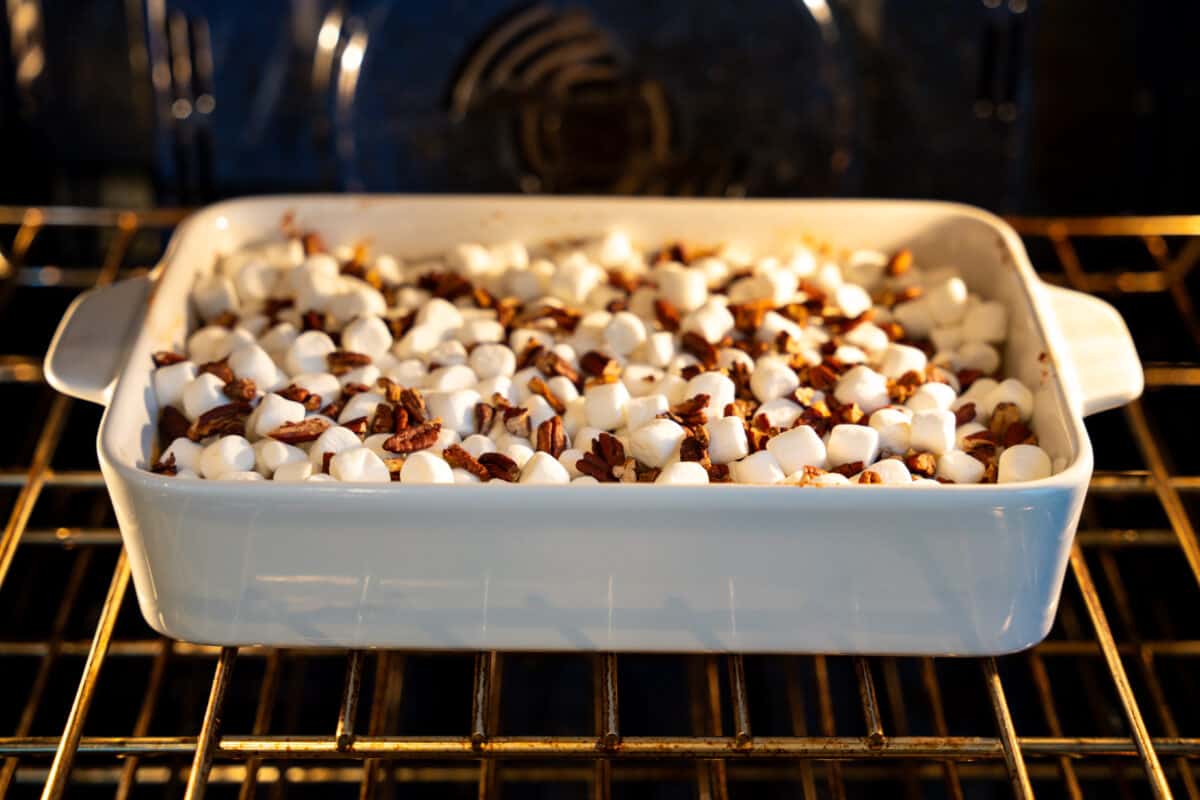 Sweet potatoe casserole topped with marshmallows and pecans in the oven