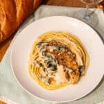 Chicken Florentine on white plate next to bread and glass of wine