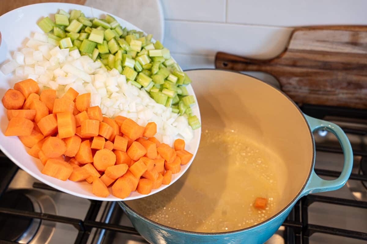chopped carrots, onion, and celery being added to pot with butter
