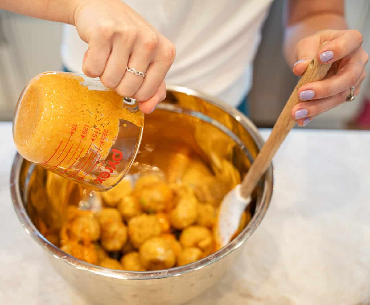 tossing buffalo chicken meatballs in buffalo sauce