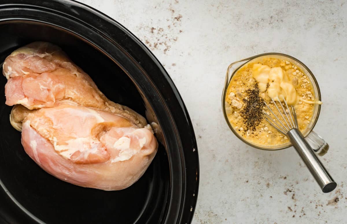 raw chicken in crock pot next to mixing bowl with gravy and whisk