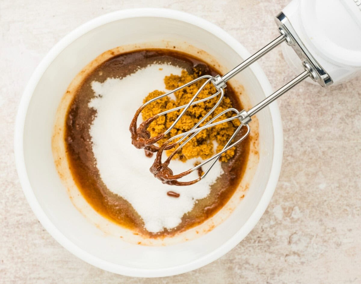 mixing in sugar to melted chocolate in bowl with hand mixer