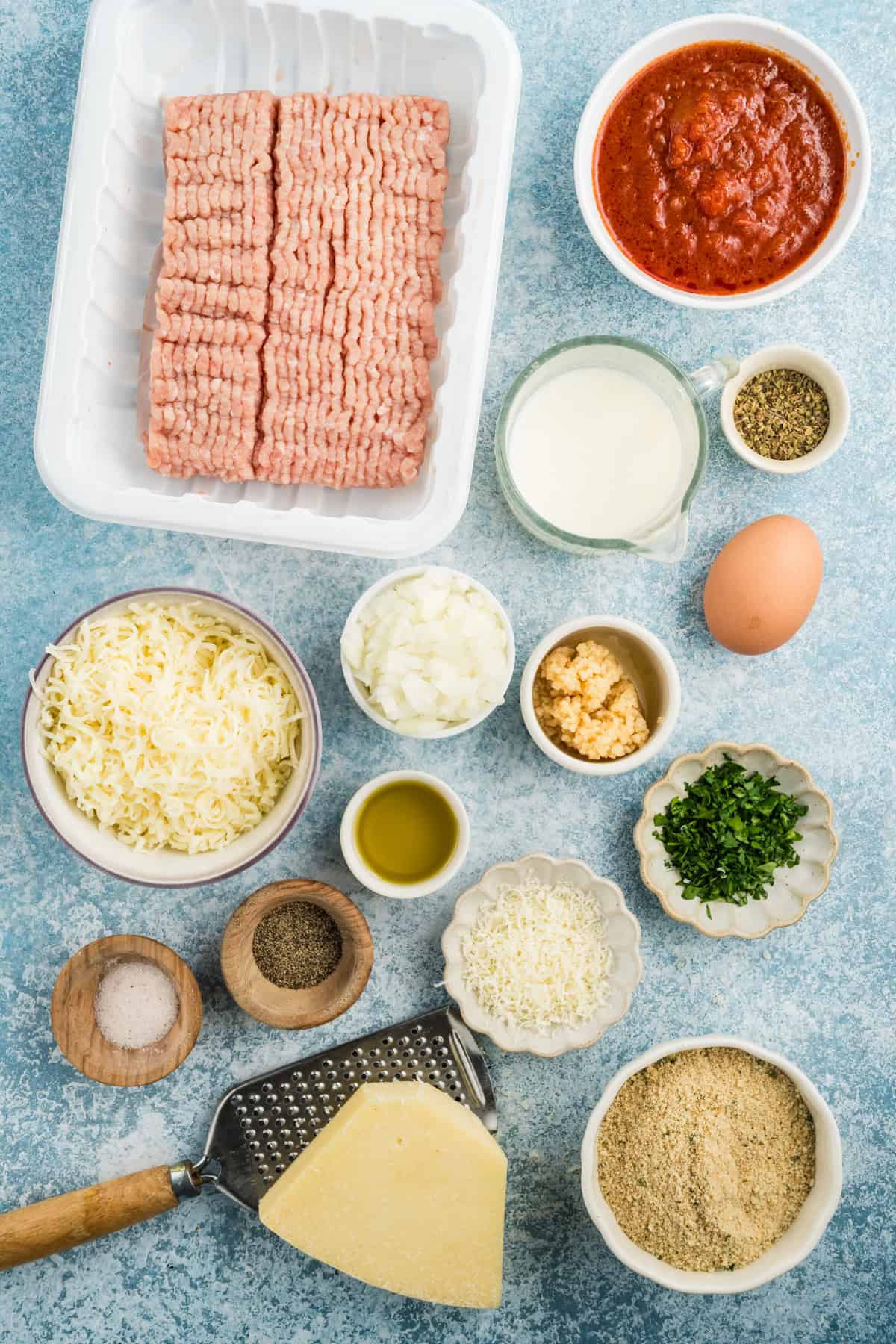 Ingredients for parmesan chicken meatloaf arranged on a blue countertop.